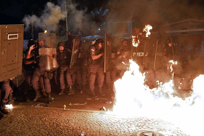 Los policías antidisturbios se protegen de cócteles molotov lanzados por manifestantes violentos en Río de Janeiro, Brasil, con motivo de las protestas por la visita del papa