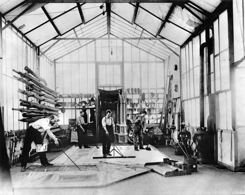 Georges Méliès pintando un decorado en el suelo de su estudio, con dibujo preparatorio en una de las manos.