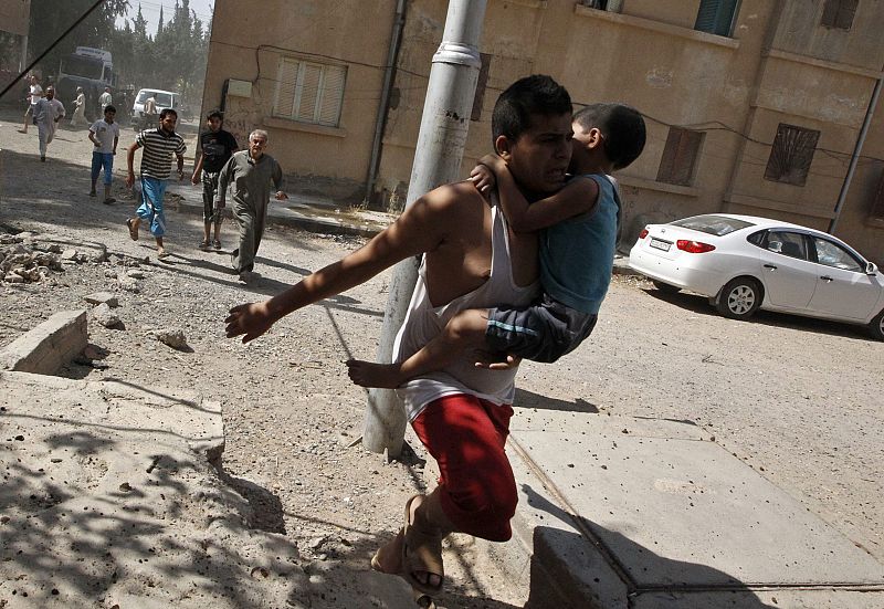 Un hombre corre con un niño en brazos en la provincia de Raqqa, al este de Siria, para refugiarse de lo que grupos activistas denuncian que es un ataque con armas químicas del Ejército sirio