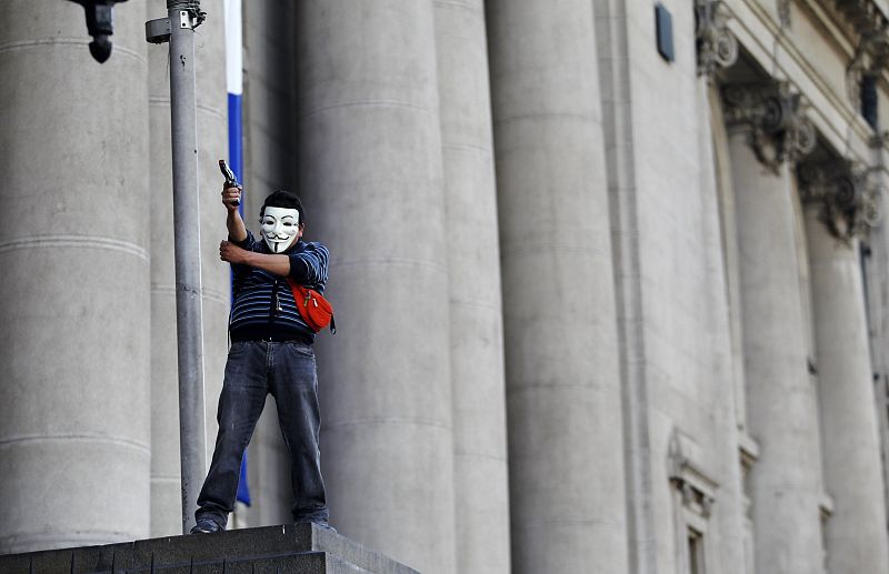 Un joven porta la máscara de Anonymus mientras sostiene una pistola de pelotas de goma.