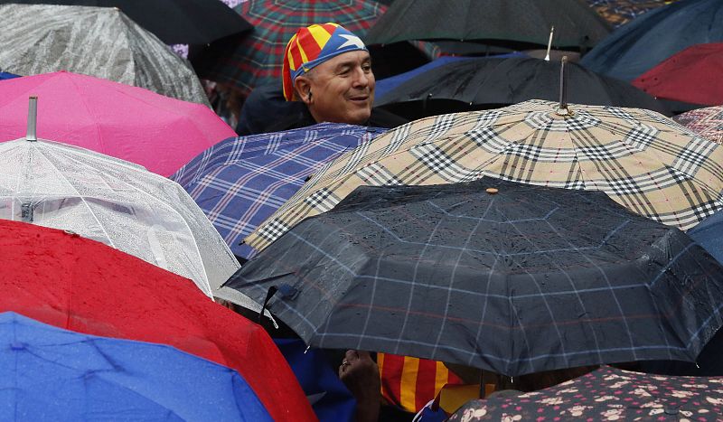 Un hombre, con una barretina y la bandera estelada, sobresale sobre los paraguas en una lluviosa mañana en Barcelona.