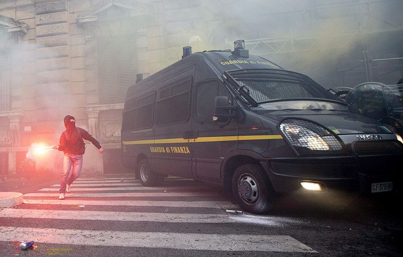 Uno de los participantes en las protestas anti-austeridad de Roma lanza una bengala durante los enfrentamientos contra la Policía