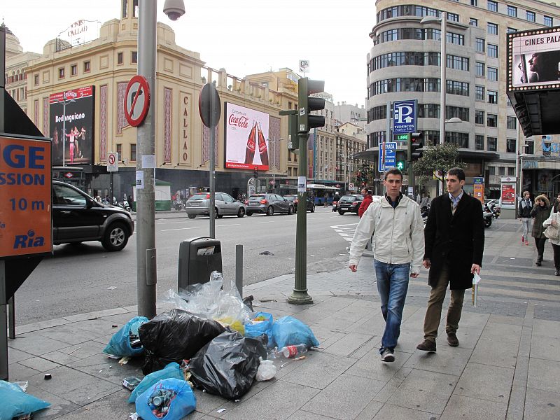 Dos ciudadanos pasan junto a varias bolsas de basura en Gran Vía