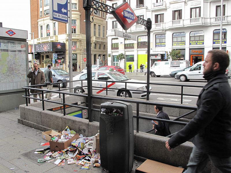 Basura en en suelo junto a una papelera en la boca de metro de Callao