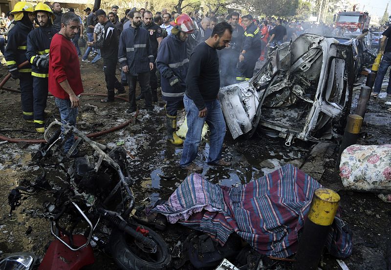 Civil Defence personnel and civilians gather at the site of explosions as a dead boy lies on the ground near the Iranian embassy in Beirut