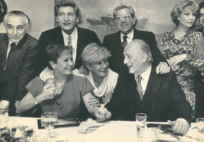 Lina Morgan sentada junto a Antonio Mingote y rodeada de actores. (1985)