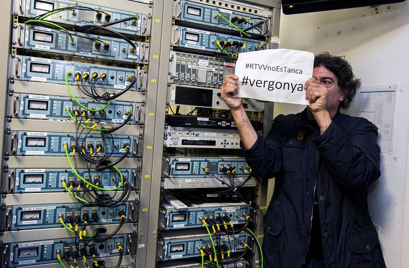 Uno de los trabajadores de RTVV muestra un cartel en protesta por el cierre inminente de Canal Nou, en la sala de control técnico.