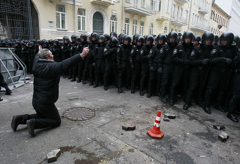 A man kneels down while riot police stand guard near the presidential administration building during a rally held by supporters of EU integration in Kiev