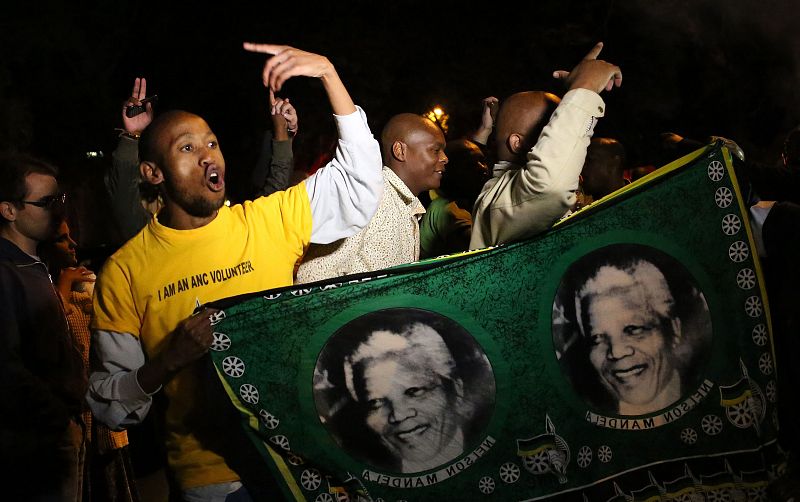 Decenas de sudafricanos sostienen fotografías e imágenes en memoria de Nelson Mandela frente a la casa en la que ha fallecido este jueves en Johannesburgo.