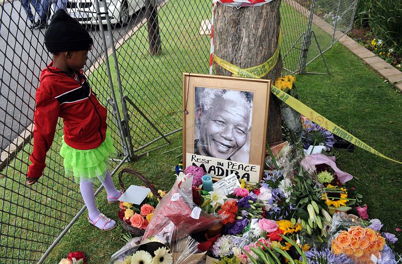 Una niña observa el retrato de Nelson Mandela y las flores que recuerdan al presidente fallecido en Johannesburgo