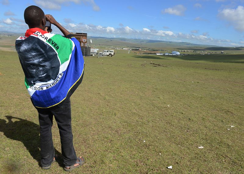 Un hombre con una bandera con el retrato de Mandela fotografía la carpa donde tiene lugar el funeral