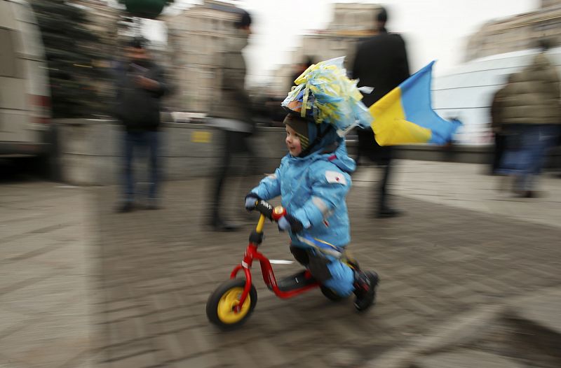 A young child carrying a Ukranian flag uses a scooter during a pro-European integration rally in Independence Square in Kiev