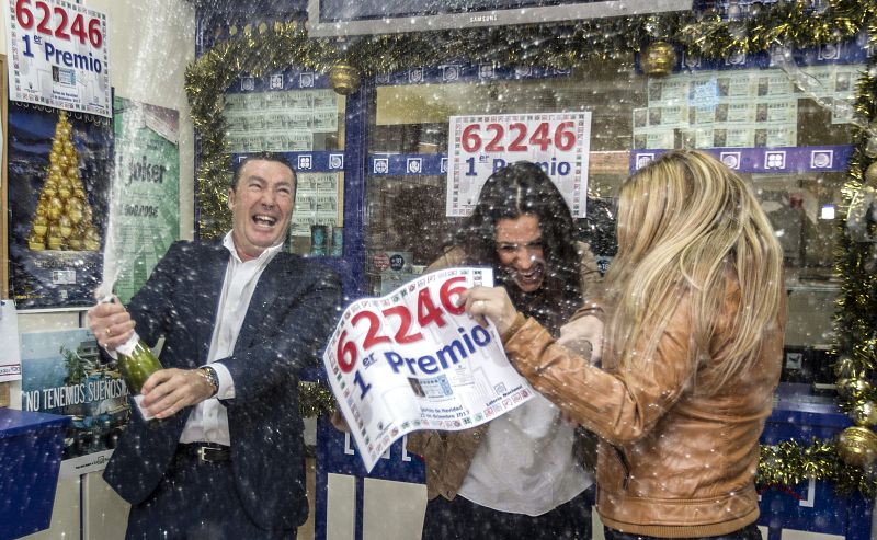 El dueño de la administración de lotería de Sanlúcar la Mayor, donde ha tocado el Gordo, descorcha una botella de champán, junto a sus empleadas.