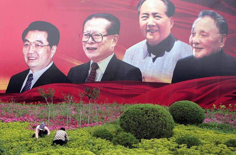 Varios obreros trabajan en un jardín con las fotos de varios líderes chinos de fondo