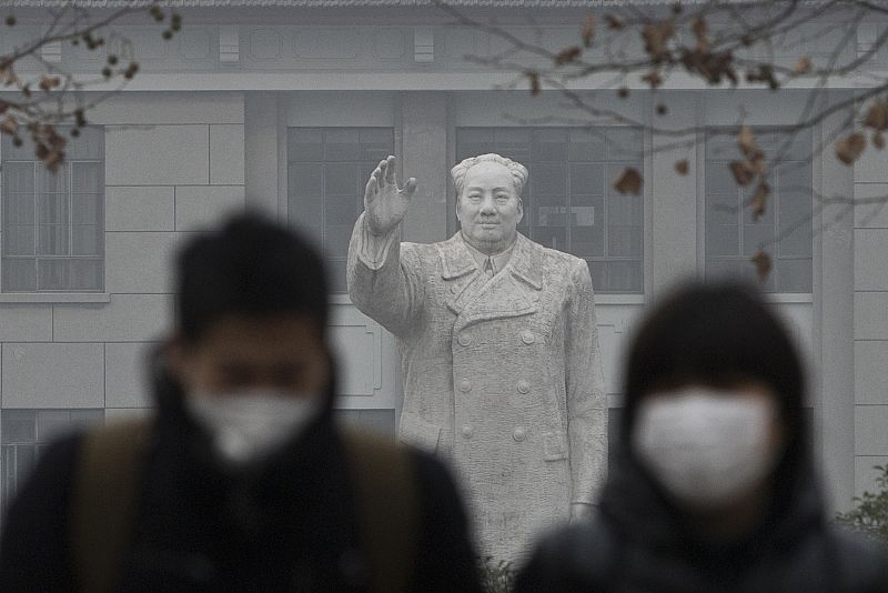 Algunos chinos con máscaras delante de la estatua del líder chino Mao Zedong