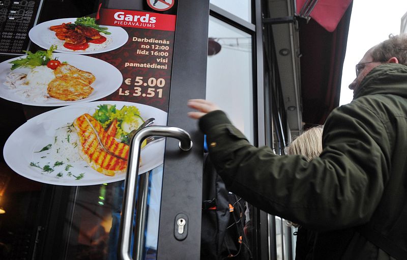 Un hombre entra en un restaurante de Riga, donde se muestran los precios en euros y lats