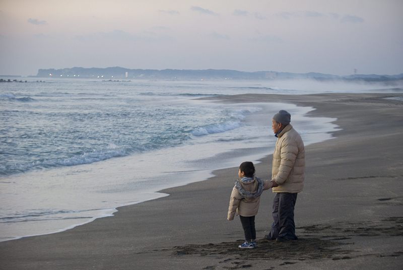 Un hombre camina con su nieto en el primer amanecer en la playa de Isumi