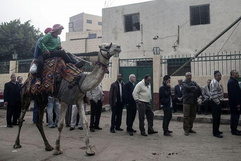 Dos jóvenes en un camello pasan al lado de una de las colas para votar en Al Haram, en el barrio cairota de Giza.