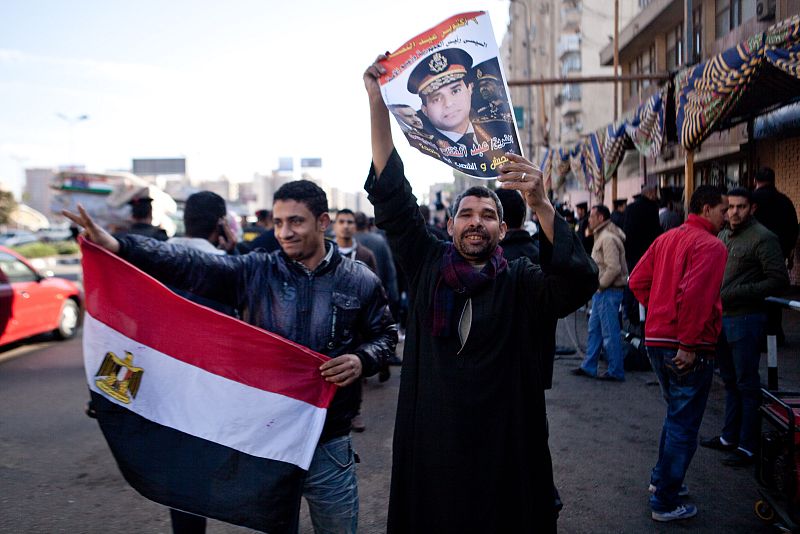 Dos hombres muestran un retraso del Ministro de Defensa, general Abdel Fattah al Sisi, frente a un colegio electoral en la capital