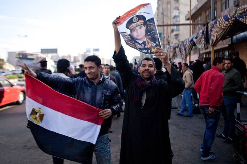 Dos hombres muestran un retraso del Ministro de Defensa, general Abdel Fattah al Sisi, frente a un colegio electoral en la capital