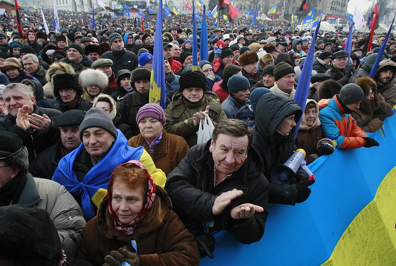 Pro-European integration protesters applaud and hold flags during a rally at Independence Square in Kiev