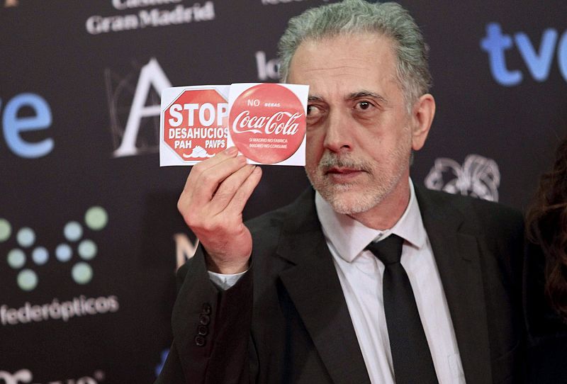 El director de cine Fernando Trueba sosteniendo pegatinas reivindicativas de 'Stop desahucios' y 'en contra del ERE de Coca Cola.