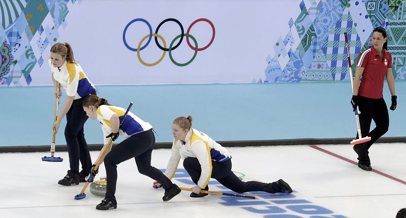 Sweden's Sigfridsson delivers a stone as third Bertrup and second Wennerstroem sweep ahead of it during their women's curling round robin game against Switzerland at 2014 Sochi Olympics