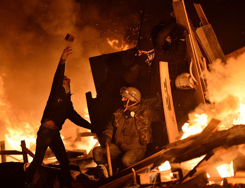 Manifestantes arrojan adoquines a la Policía protegidos tras una barricada incendiada