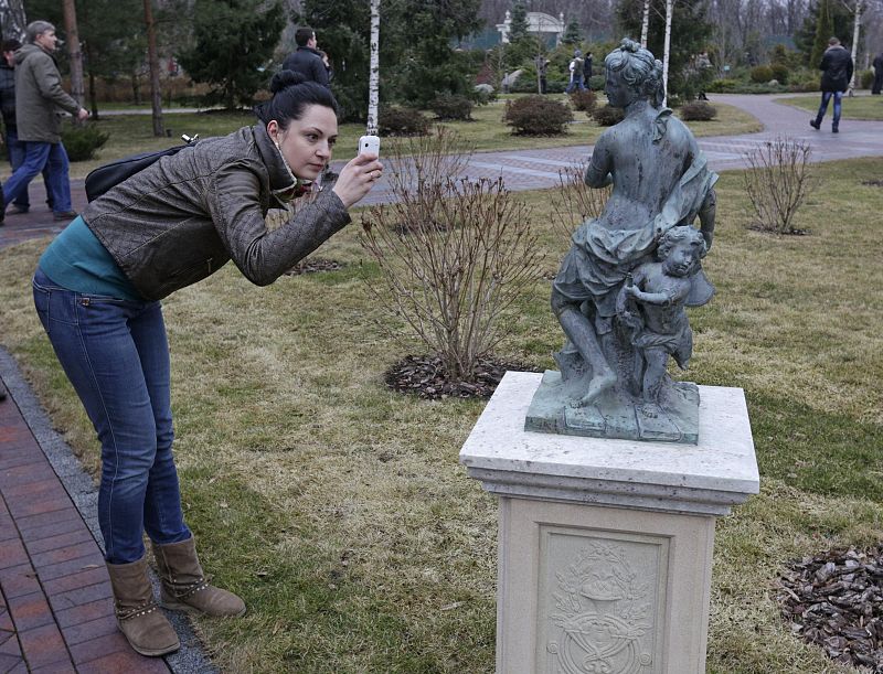 A woman takes a picture of a statue as anti-government protesters and journalists walk on the grounds of the Mezhyhirya residence of Ukraine's President Viktor Yanukovich in the village Novi Petrivtsi outside Kiev