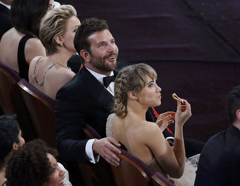Bradley Cooper, nominado a mejor actor secundario por 'La Gran Estafa Americana' junto a su novia, Suki Waterhouse, que come pizza durante la ceremonia.