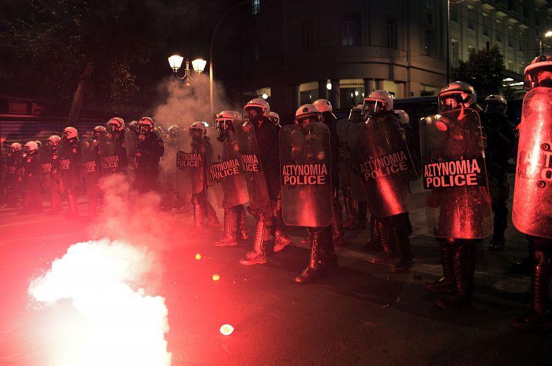 Los agentes antidisturbios avanzan ante una bengala en el centro de Atenas