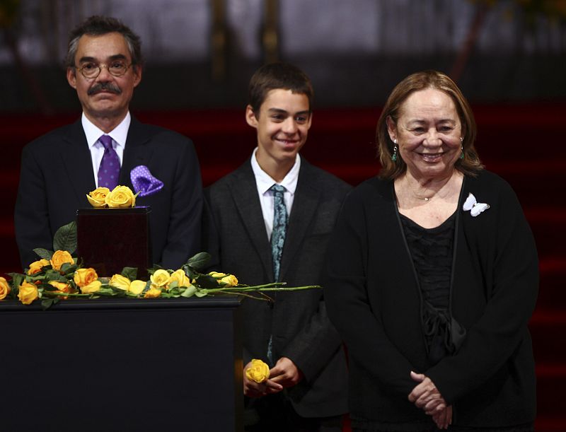 Las flores amarillas, las preferidas por el autor y que solía utilizar para adornar su solapa cuando aparecía públicamente han estado presentes en su homenaje. En la imagen su viuda acompañada por su hijo Gonzalo y su nieto.