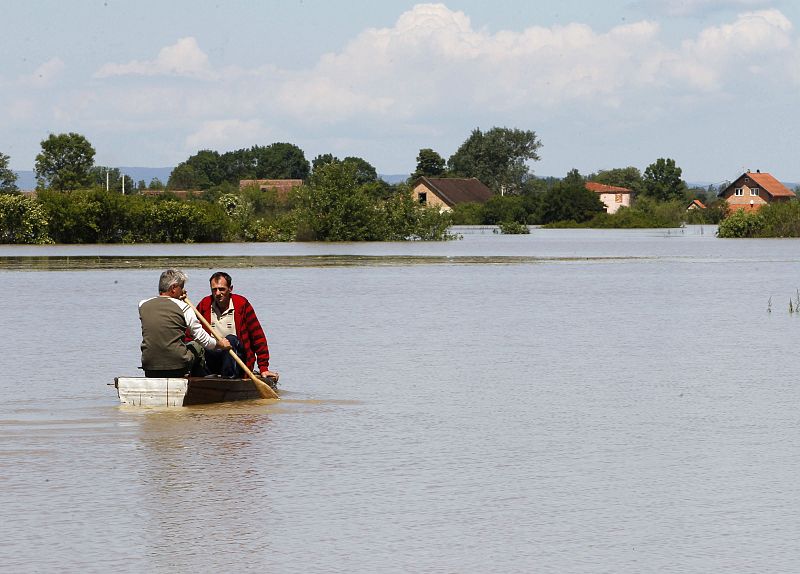 Men paddle towards homes during heavy floods in the village of Vojskova