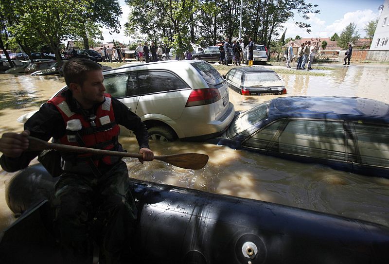 A man paddles his boat past cars soaked in flood water in Obrenovac