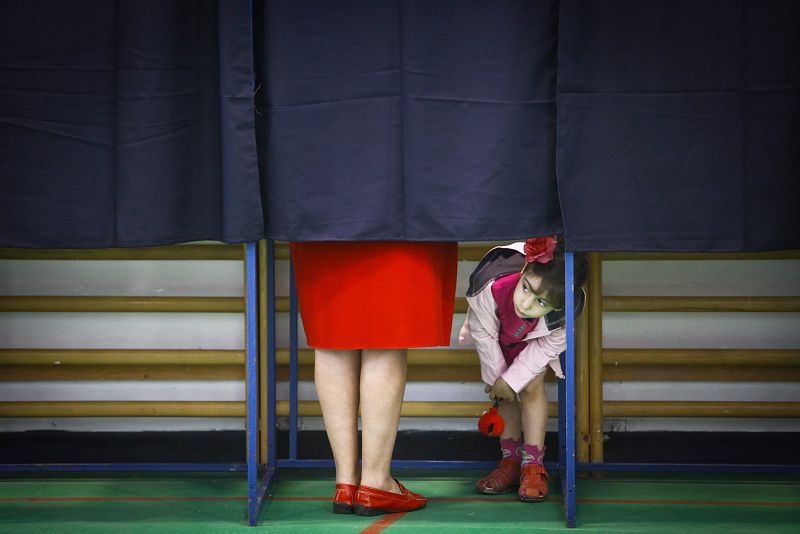 Una niña se asoma desde una cabina de votación en un colegio electoral en Bucarest (Rumania).