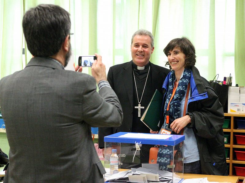 Una mujer que acude a votar se hace una fotografia con el obispo de Bilbao, Mario Iceta, que preside una mesa de un colegio electoral en Bilbao.