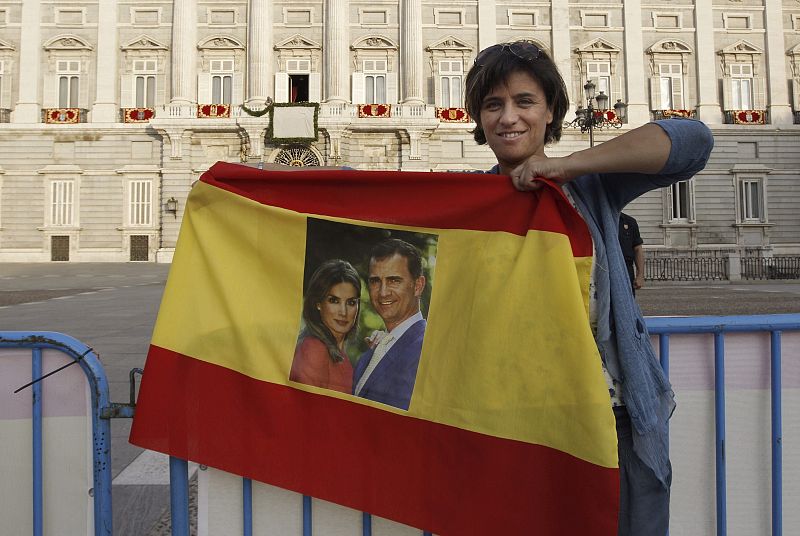 Una mujer sostiene una bandera con la fotografía de los reyes, ante el balcón central del Palacio Real