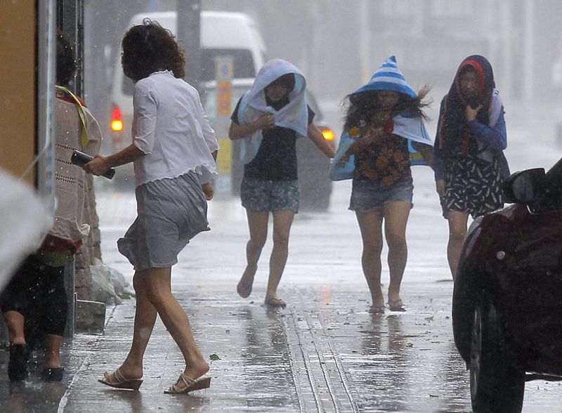 Mujeres caminan en medio de fuertes vientos en una calle comercial de Naha, Okinawa.