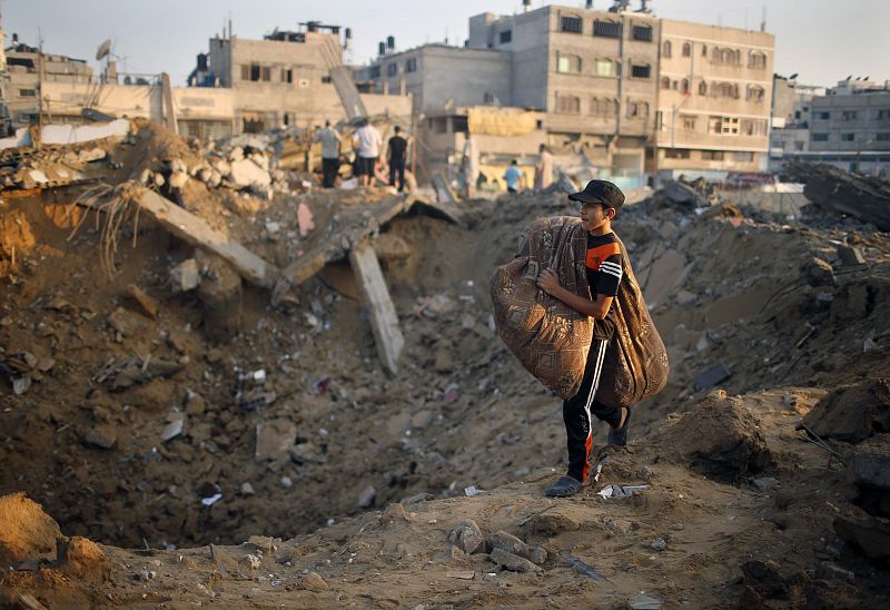 Un joven palestino carga sus pertenencias mientras camina sobre las ruinas de su casa, destruida en el ataque israelí en la ciudad de Gaza.