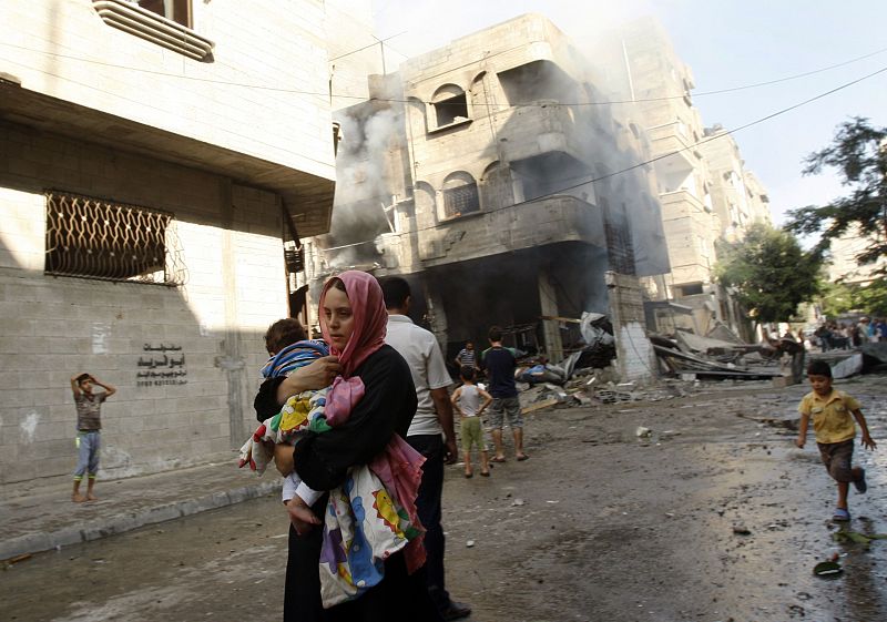 Una mujer palestina huye con su hijo en brazos de un edificio bombardeado durante la operación militar "Margen Protector"