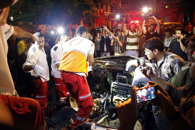 Un equipo de asistencia sanitaria palestino revisan un coche destruido, cuyo conductor falleció a causa de los bombardeos