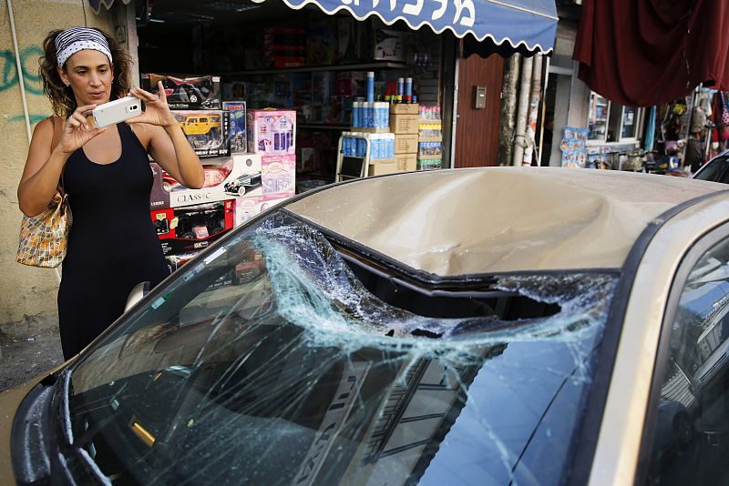 Una mujer toma con su teléfono móvil en un vecindario de Tel Aviv una fotografía de un coche dañado por los restos de un cohete interceptado por IsraelIsrael landed in Tel Aviv