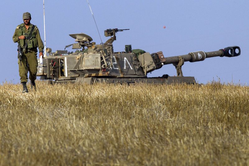 Un soldado israelí camina junto a un cañón de artillería móvil estacionado en la frontera sur de Israel con la Franja de Gaza.