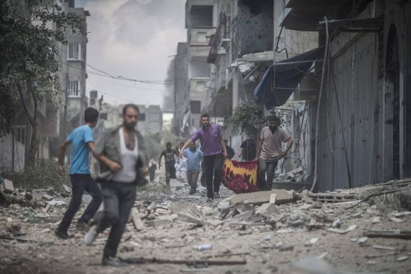 Dos palestinos llevan a una persona muerta y huyen de sus hogares durante la tregua humanitaria.