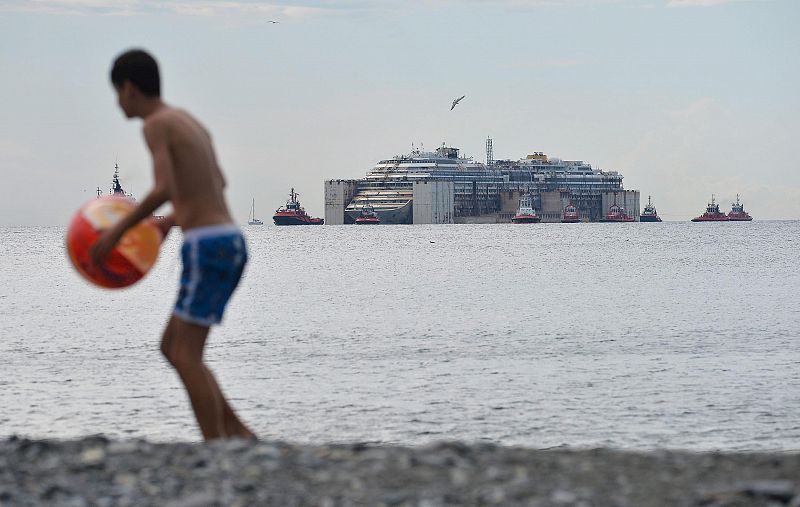 Un chico juega en la playa donde puede verse la llegada del Costa Concordia