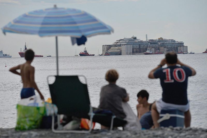 Varias personas miran desde la playa de Génova (Italia) la llegada del Costa Concordia.