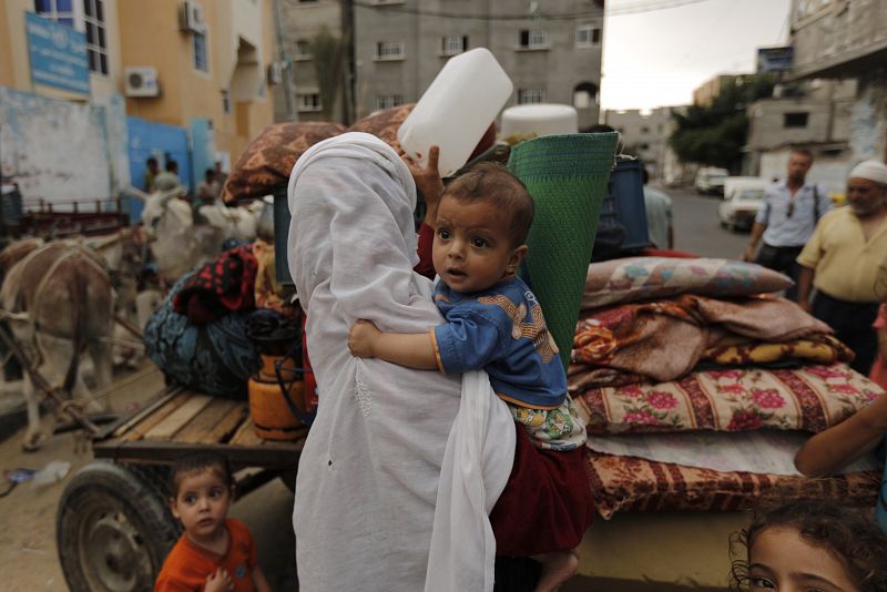 Una mujer palestinada con su hijo en brazos carga sus pertenencias en un carro en el que su familia viajará hasta su hogar durante la tregua