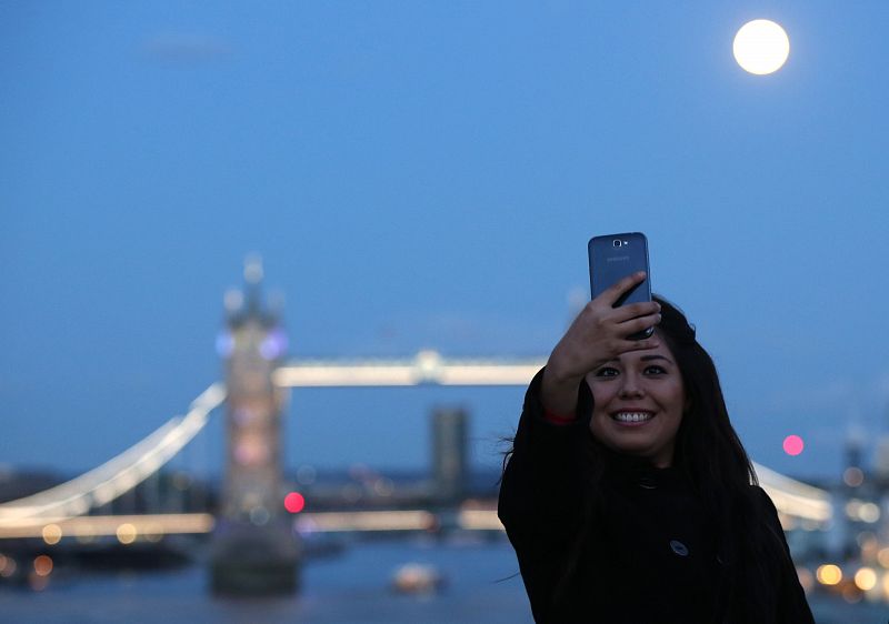 Una mujer toma un 'selfie' con la superluna y el Tower Bridge londinense de fondo.