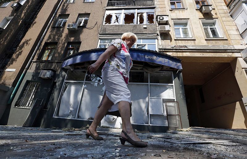 Una mujer camina al lado de un edificio dañado por los bombardeos