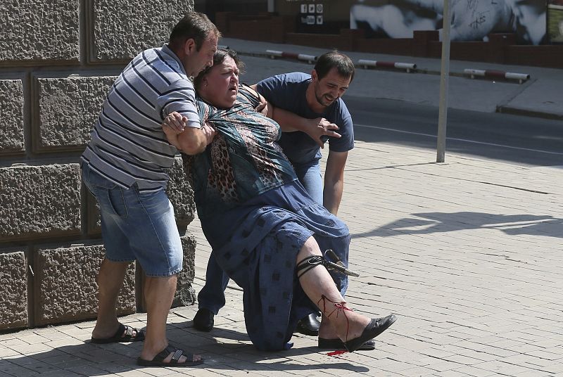 Dos hombres ayudan a una mujer que ha resultado herida el ataque con proyectiles de artillería